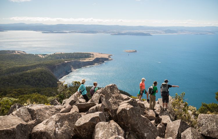 Guests atop rocks overlooking Wineglass Bay and ocean