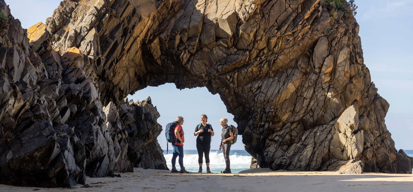 Guests standing on beach under Bruny Island Rock formation
