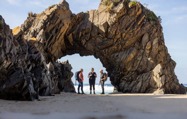 Guests walking along the beach standing under rock feature